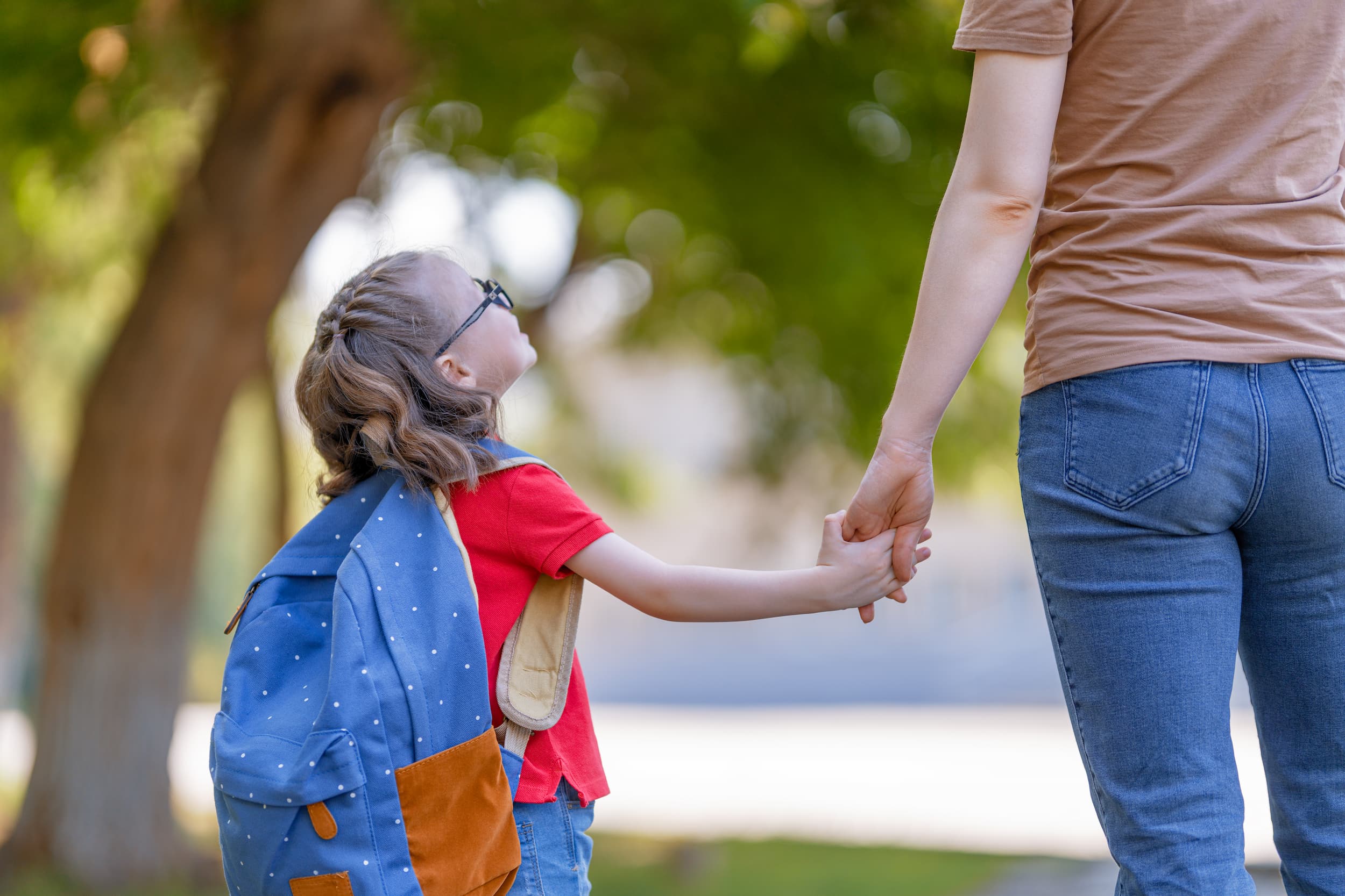 Mother and child hold hands walking into school.